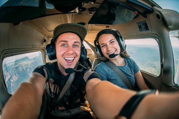 Two Cheerful Young Adult Friends Together in the Cockpit Flying a Small Single Engine Airplane Wide Angle Selfie Fisheye Shot of Two Cheerful Young Adult Male and Female Friends Together in the Cockpit Flying a Small Single Engine Airplane airplane hangar photos stock pictures, royalty-free photos & images