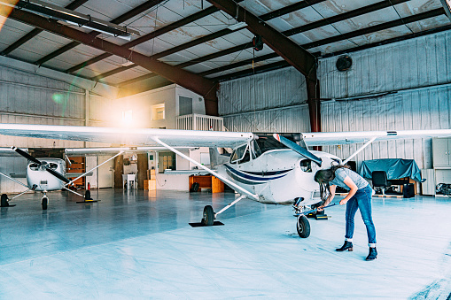 Young Adult Female Pilot Wearing High Heels Preparing to Move a Small Single Engine Airplane Out of Hangar Storage