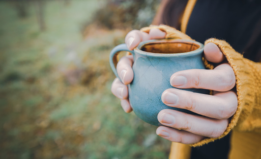Young woman hands holding a blue mug of tea outdoor. Seasonal concept. High quality photo