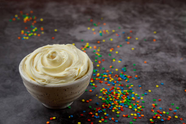 Butter cream and sprinkles in bowl on dark background.