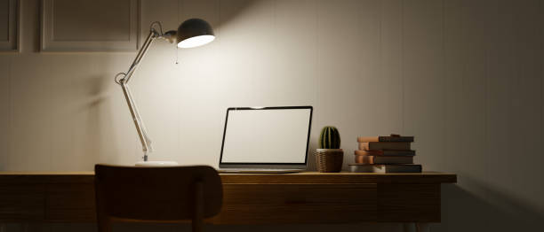 istock Home office space at night with low light, tablet with blank empty screen, modern table lamp, mock up frame 1330143323