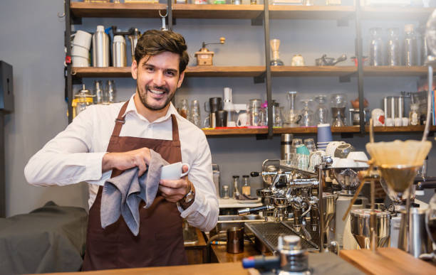 startup de sucesso sme pequeno negócio empresário proprietário homem limpeza copo em sua cafeteria ou restaurante. retrato de jovem caucasiano bem sucedido dono de café barista dentro de casa. - indian culture manager men asian ethnicity - fotografias e filmes do acervo