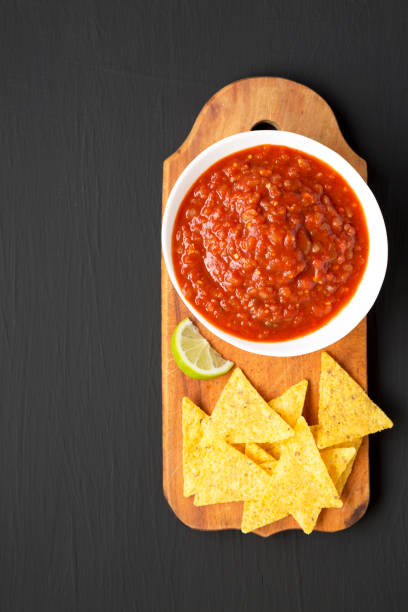 istock Homemade Tomato Salsa and Nachos on a rustic wooden board on a black surface, overhead view. Flat lay, top view, from above. Space for text. 1330154574