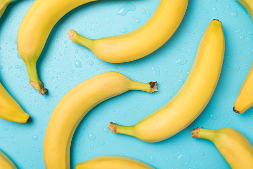 Top view photo of unpeeled yellow bananas and drops of water on isolated pastel blue background