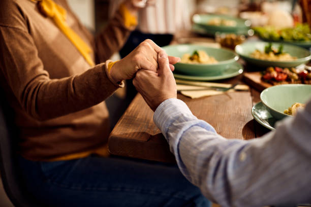 Close-up of friends saying grace before the meal at dining table. Close-up of people holding hands and praying while sitting at dining table. saying grace stock pictures, royalty-free photos & images