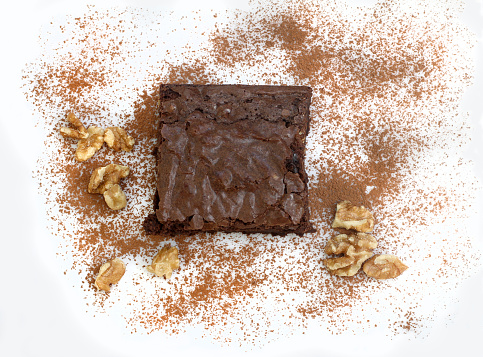 Top view of a chocolate fudge and walnut brownie surrounded with sprinkled cocoa and walnuts.