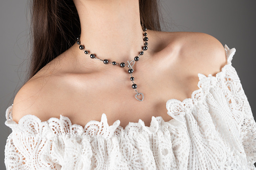 Cropped shot of a woman with chain necklace made of hematite. The lady with a naked collarbone and shoulders wears white dress. High quality photo