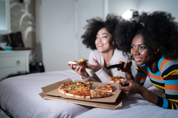 istock African women lying down on bed, eating pizza and watching TV. 1330161355