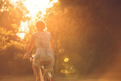Copy space shot of mature woman in a sundress sitting on her bike and riding into the sunset.