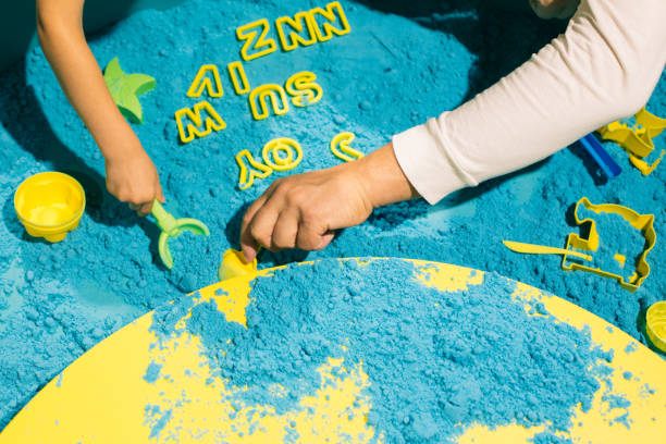 mains d’enfants et d’adultes jouant avec du sable cinétique bleu. art-thérapie. soulager le stress et la tension. sensations tactiles. développement de la motricité fine. concentration et attention. - sandbox child human hand sand photos et images de collection