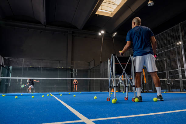 monitor ensinando aula de padel para o homem, seu aluno - treinador ensina menino como jogar padel em quadra de tênis interior - tennis men indoors playing - fotografias e filmes do acervo