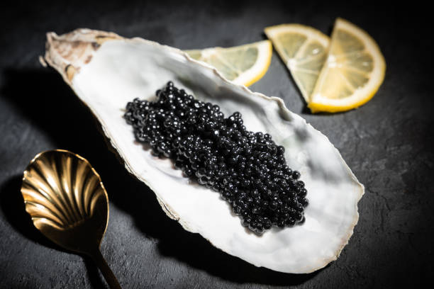 Black caviar in oyster shell on black slate background Black caviar in oyster shell on black slate background roe river stock pictures, royalty-free photos & images