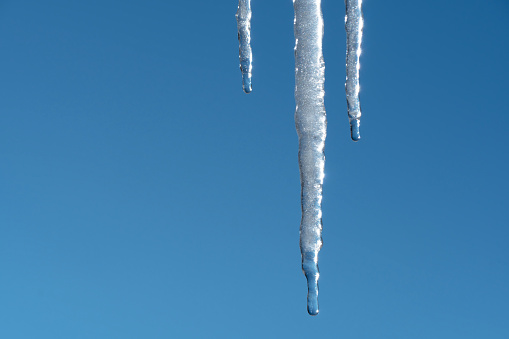 Icicles melt and drip in the spring against the blue sky.Meteorology, global warming, and melting snow and ice. Water dripping against the sky.