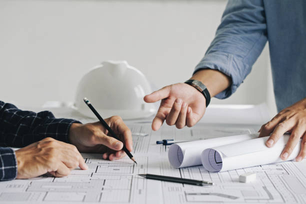 Two business man construction site engineers. working drawing on blueprint and discussing the floor plans over blueprint architectural plans at table in a modern office. construction concept stock photo