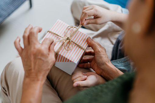 Close up of hand of a grandmother and grandchild opening a gift box
