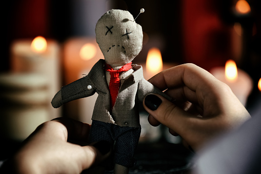 Woman holding voodoo doll with pins indoors, closeup. Curse ceremony