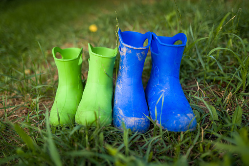 Close up color image depicting two pairs of dirty, muddy children's rubber boots outdoors in the yard. One pair is blue and the other is a vibrant lime green. Room for copy space.