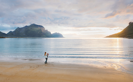 Woman walking with child on sandy beach family vacation traveling in Norway summer trip outdoor mother with baby enjoying sunset ocean and mountains view