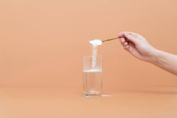 la mano vierte proteína de colágeno en polvo en un vaso de agua sobre un fondo beige. un suplemento natural para la belleza de la piel y la salud ósea. - dissolving fotografías e imágenes de stock