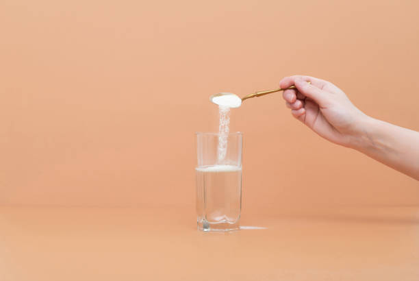 Hand pours collagen protein powder in a glass of water on a beige background. A natural supplement for skin beauty and bone health. Hand pours collagen protein powder in a glass of water on a beige background. A natural supplement for skin beauty and bone health. Space for text. human collagen stock pictures, royalty-free photos & images