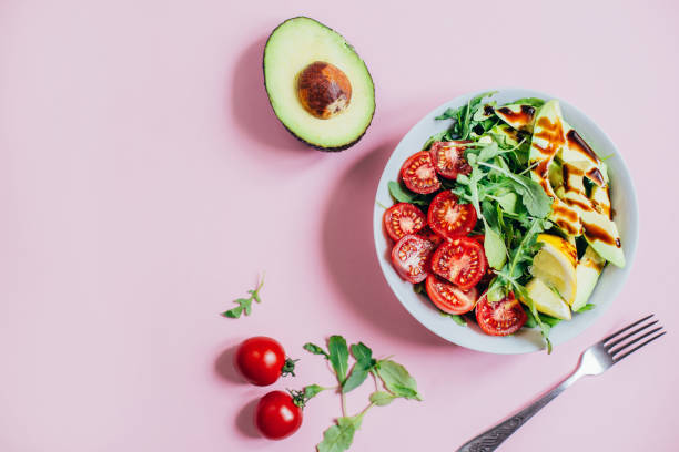 ピンクの背景に白いプレートでトマトサラダルッコラアボカドレモンのトップビュー - appetizer lunch freshness vegetable ストックフォトと画像