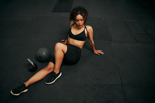 African American female athlete resting after an intense workout in the gym. Sporty woman holding skipping rope. High quality photo