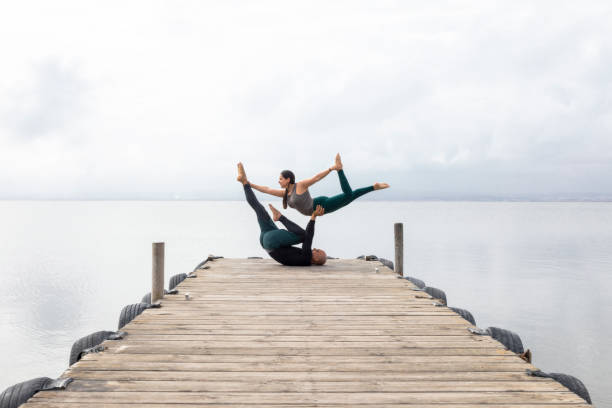 para praktykujących akrojogę na drewnianym doku na jeziorze - yoga flexibility two people women zdjęcia i obrazy z banku zdjęć