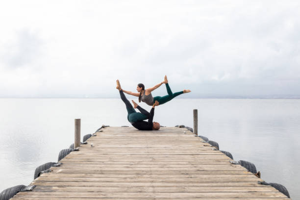 пара, занимаюсь акройогой на деревянном причале на озере - yoga flexibility two people women стоковые фото и изображения