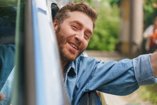 istock A happy smiling man waving to someone while driving a car 1330182636