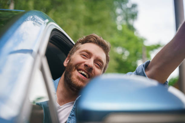 A middle aged man waving to someone while driving a car