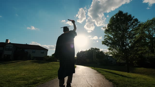 Rear view of the university graduates student at Silhouette sunset goes on the road. Slow motion