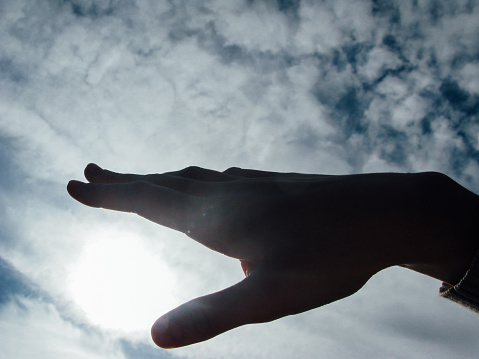 Hand doing gestures with the sun and cloudy sky background. Concept of abstract.