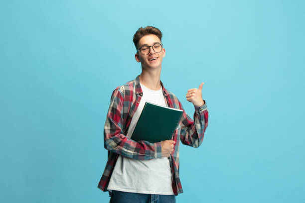 istock Half length portrait of young caucasian guy, student with notepad isolated over light blue studio background. 1330196890