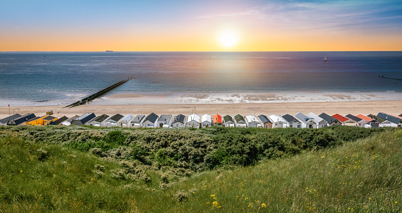 Panoramic view of beautiful beach with a row of beach huts. Sunset sky. One of the most beautiful beaches in Dishoek, Zeeland, The Netherlands. Summer travel destination.