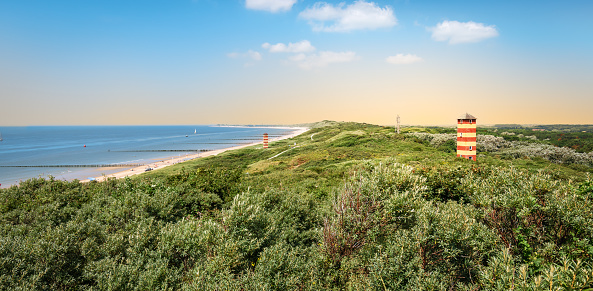 Panoramic view of beautiful beach and lighthouse in the dunes during sunset. Blue sky. Bright image. One of the most beautiful beaches in the Netherlands, Dishoek, located between Vlissingen and Zoutelande in the province of Zeeland. Summer travel destination.