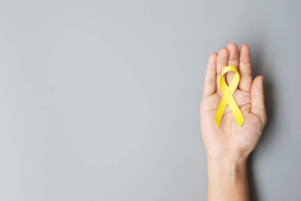 小児がん、肉腫、骨、膀胱および自殺予防啓発月間、生活と病気の人々を支援するためのゴールドイエローリボン。子供のヘルスケアと世界の癌の日の概念 - world in hands ストックフォトと画像
