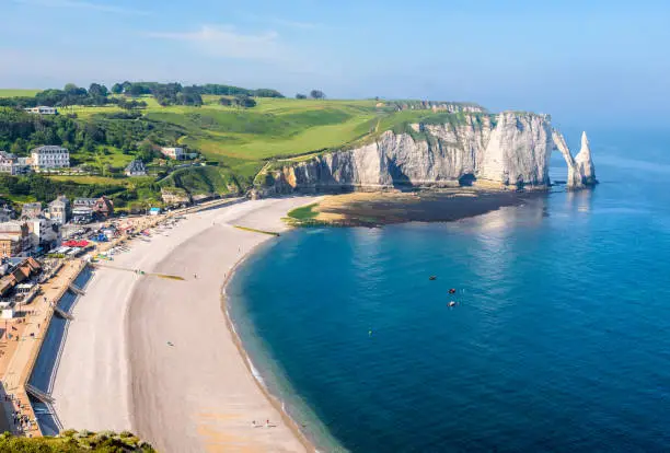 High angle view of the waterfront and pebble beach of Etretat in Normandy with the Needle and the arch of the Aval cliff in the distance on a sunny spring morning.