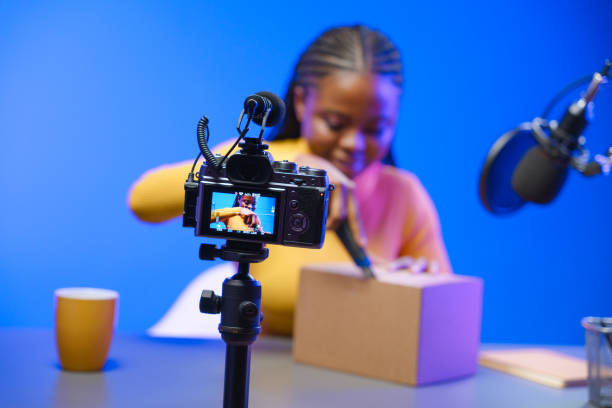 una ragazza vlogger dalla pelle scura nel suo studio inizia a disimballare una scatola di cartone. - unboxing foto e immagini stock