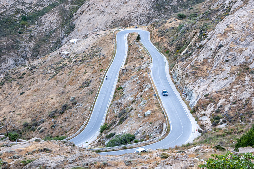 Serifos island, Cyclades Greece. High angle view of curved main road on mountains that connects two villages. Rural transport cars speed asphalt explore travel rocky hill background summer sunny day.