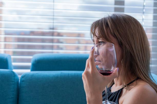 mulher sentada no sofá em sua sala de estar, bebendo um vinho tinto enquanto deitada em seu sofá desfrutando de uma tarde tranquila - home interior cocktail bar women - fotografias e filmes do acervo