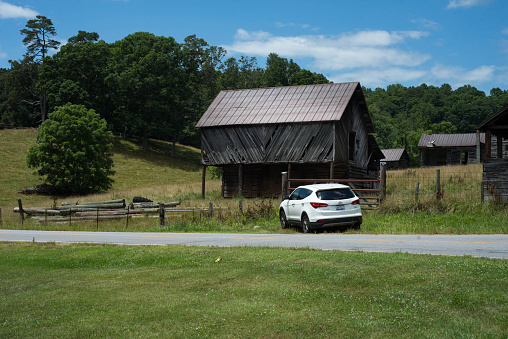 Marshall, NC, USA.  July 11, 2021.  A rural scene with a barn and other old buildings.  In front of the barn is a white SUV.  Pastures and green fields surround the buildings.