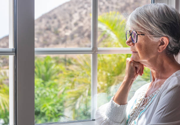 istock Pensive elderly woman at the window looking out 1330219521