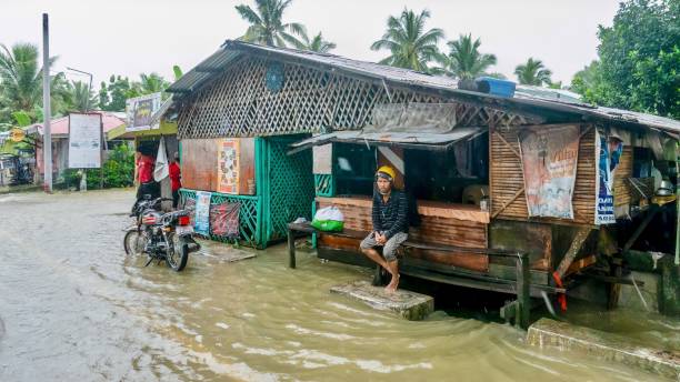 Extreme weather causes flooding on Mindoro Island in the Philippines. Baco, Oriental Mindoro, Philippines - July 23, 2021. Heavy monsoon rains flood a local restaurant along the National Highway, where a Filipino man sits on a bench in the rain. typhoon stock pictures, royalty-free photos & images