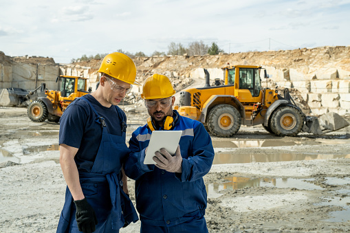 Dos constructores en ropa de trabajo mirando boceto en la pantalla de la tableta photo