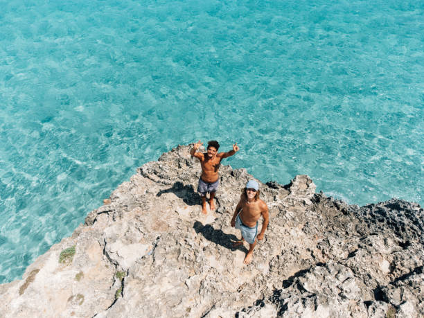 deux amis lèvent les yeux, disant bonjour au drone - swimwear caribbean sea beach water photos et images de collection