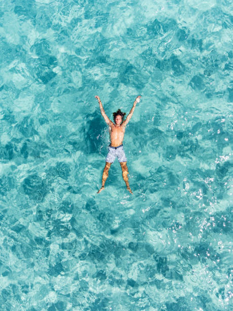 vue aérienne d’un homme se relaxant dans une belle mer turquoise transparente - floating on water swimming pool men water photos et images de collection