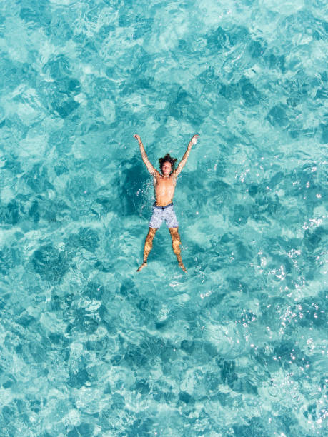 vista aérea de um homem relaxando-se em um belo mar turquesa transparente - floating on water swimming pool men water - fotografias e filmes do acervo