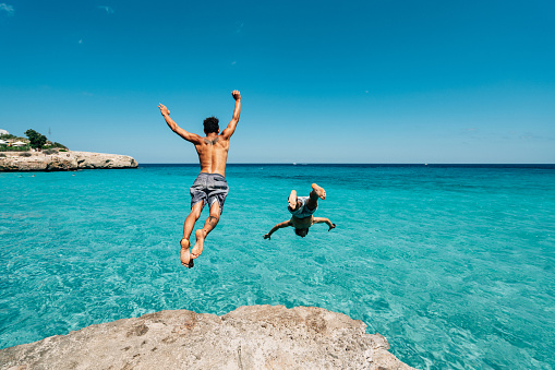 Two friends are diving in the sea from a cliff. Carefree, freedom, vacation concept.