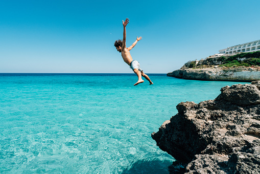 Young man is diving in the sea from a cliff. He has arms and legs outstretched.