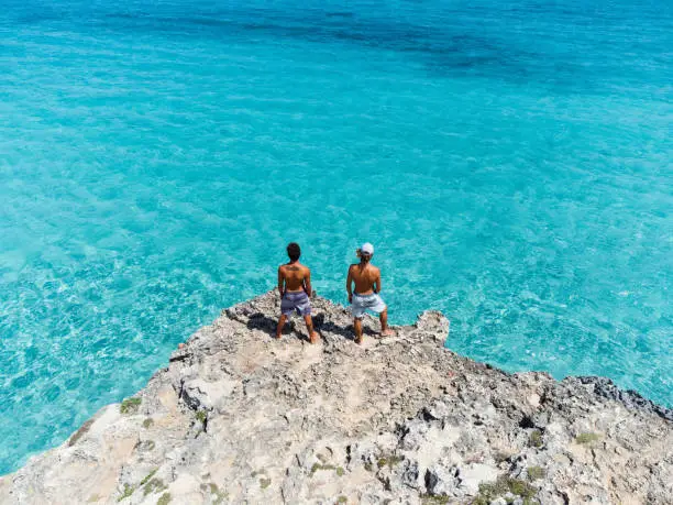 Photo of Two friends together on a cliff near a turquoise sea
